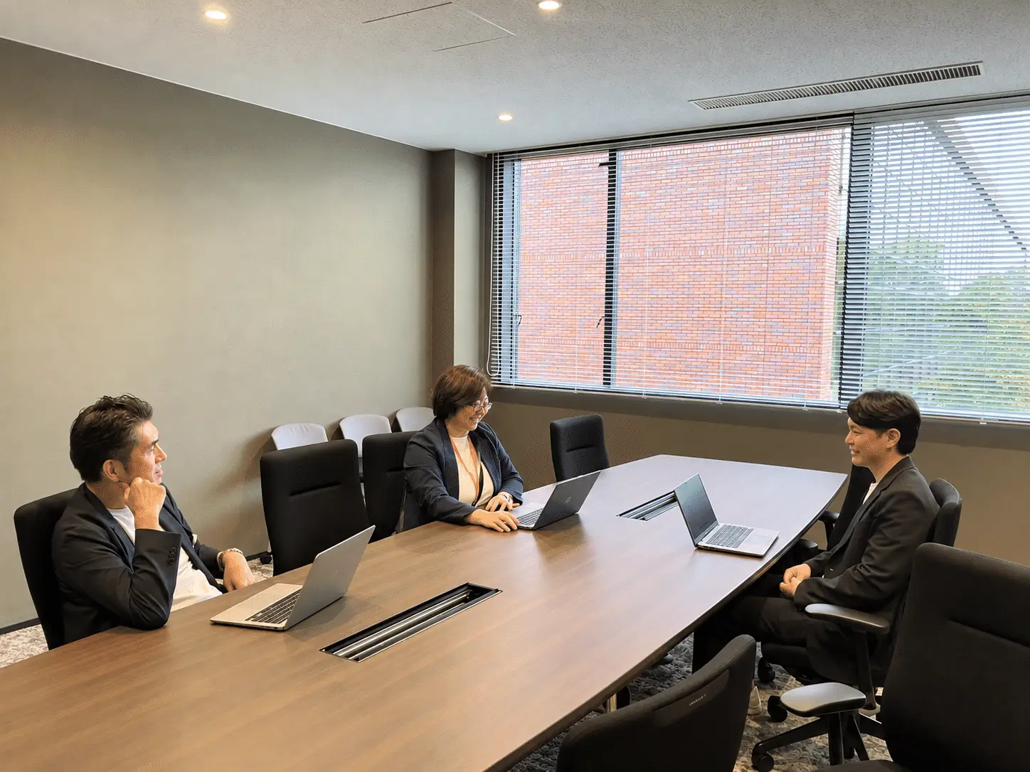 会議室の長いテーブルを囲んで話す3名